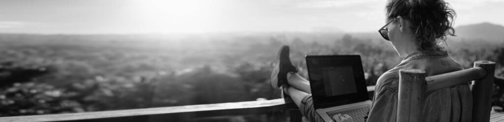Background image of person relaxing in scenic locations with feet up, reading off a laptop.
